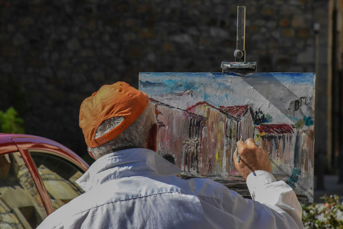 An elder man paints oil color on canvas
