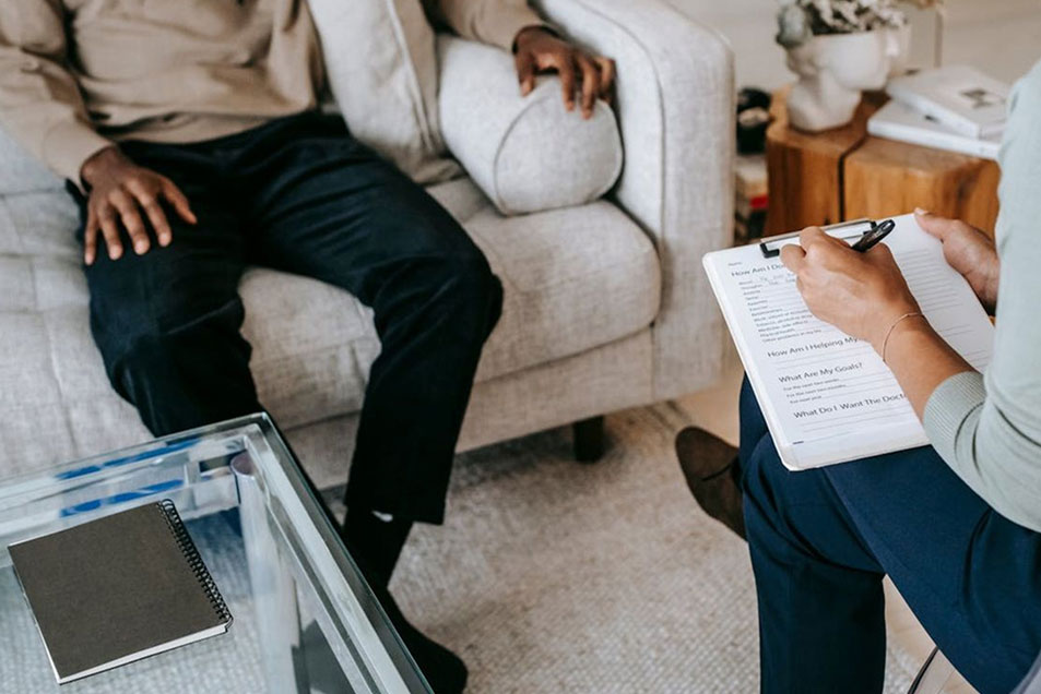 Image of a left handed woman seemingly asking a man on the couch questions while she fills out a form